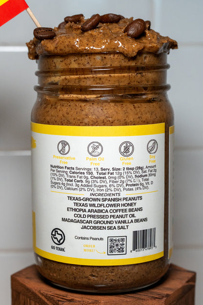 Jar of espresso peanut butter with an ingredient label, placed on a wooden block against a white tiled wall.