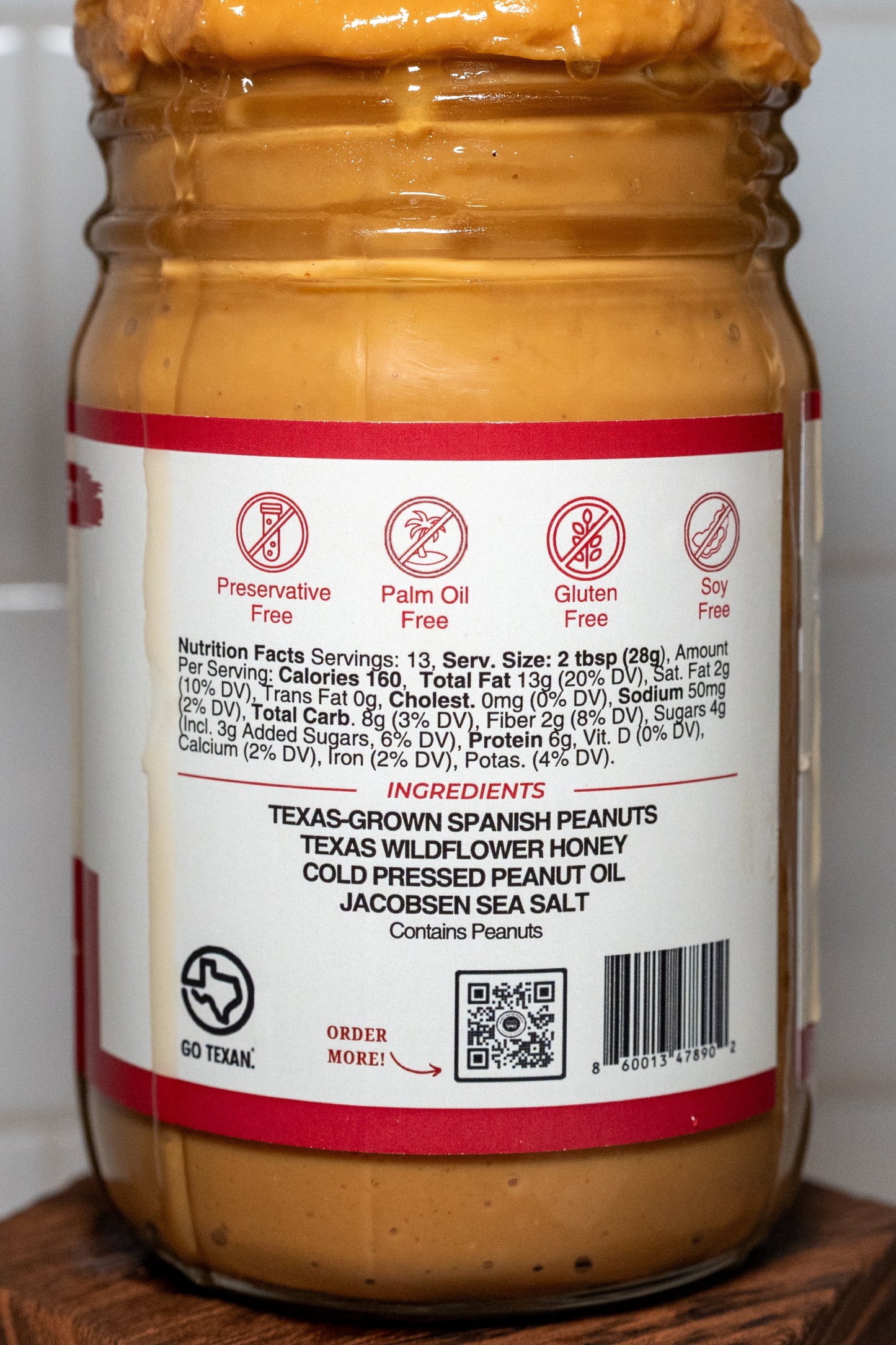 Jar of Texas honey peanut butter with a small American flag on top, against a tiled wall background.